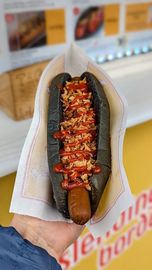 vegan hot dog covered in siracha and jalapenos in a black charcoal bun in akureyri iceland