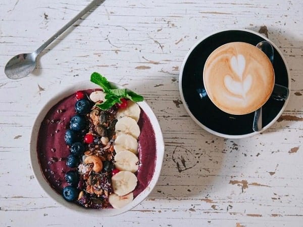 vegan acai bowl topped with bananas and blueberries next to a latte at funk you natural cafe in berlin