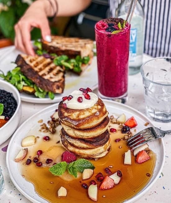 a mini stack of golden vegan pancake next to a purple smoothie and a grilled sandwich at brunch in berlin