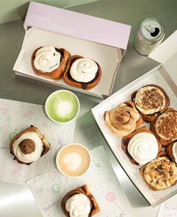 two boxes of vegan cinnamon rolls next to a latte and matcha drink on a table at have a roll in amsterdam