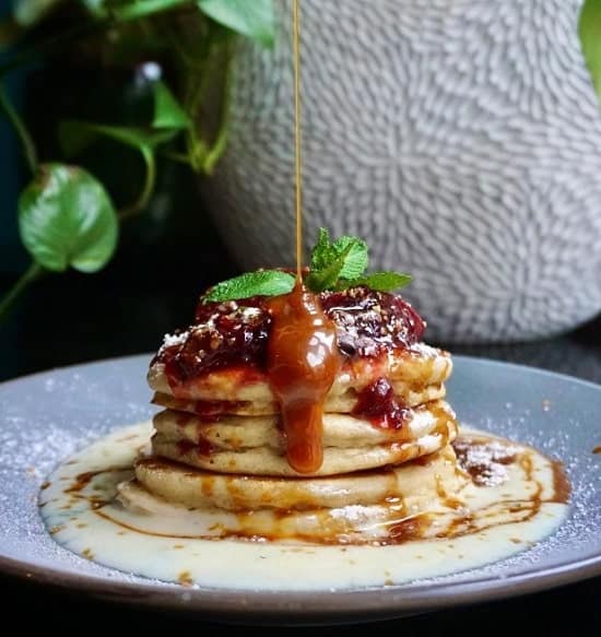 a stack of golden vegan pancakes topped with syrup and berries at manna in berlin