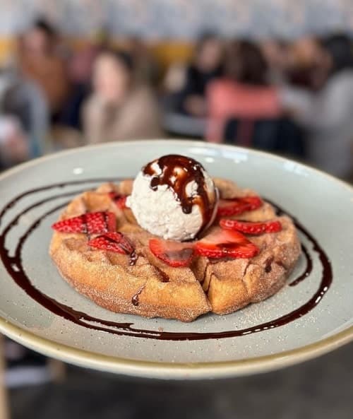 a single golden vegan belgian waffle topped with strawberries, whipped cream and chocolate sauce on a white plate at good morning kitchen las vegas
