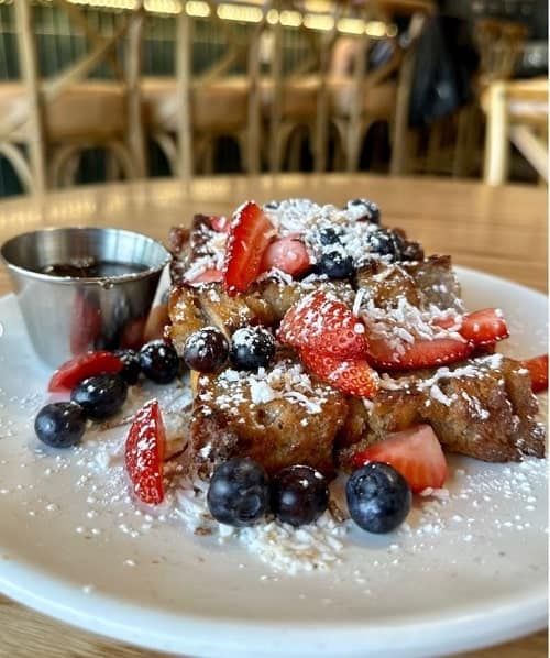 vegan breakfast french toast bread pudding topped with strawberries, blueberries, and powdered sugar from graze kitchen in las vegas