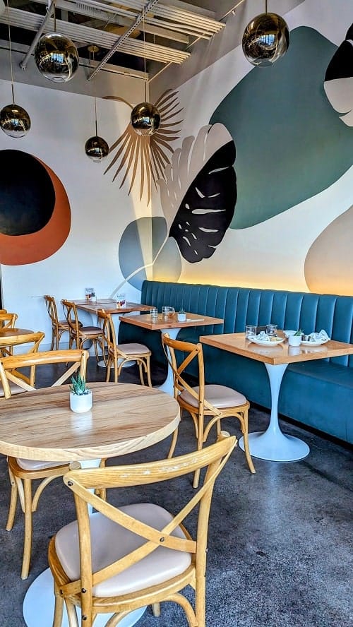 inside of the modern vegan resturant graze kitchen with light wood tables, and colorful paintings on the wall