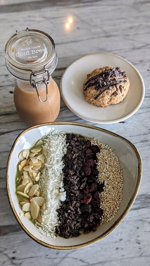a green smoothie bowl topped with coconut, nuts, and seeds next to a coffee and a cookie at the palmaia resort in playa del carmen