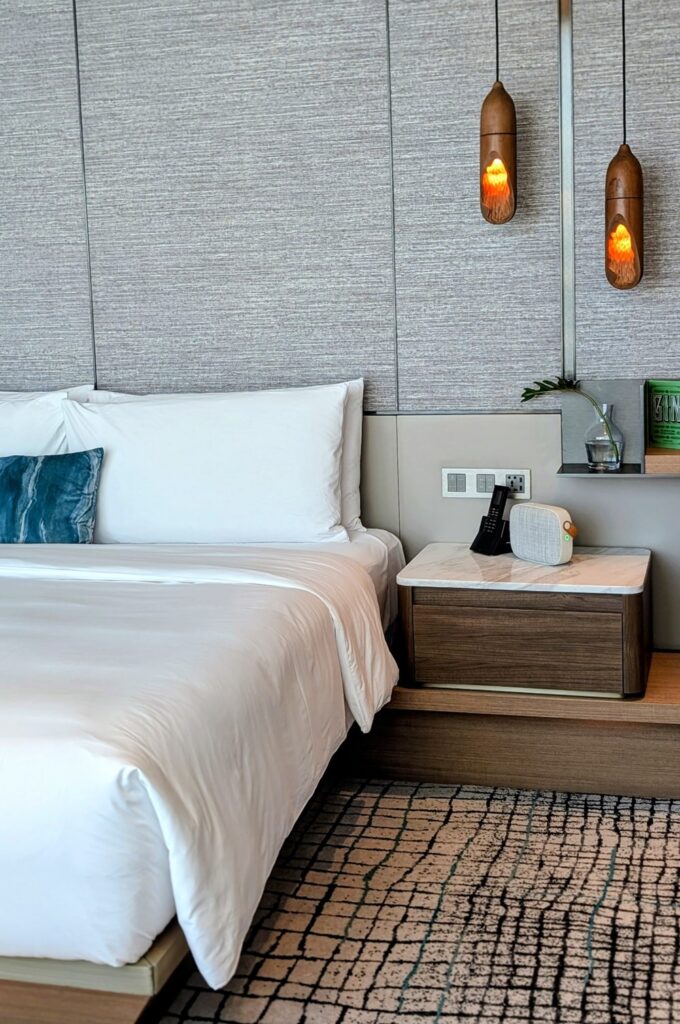 king bed with white linen and hanging wood lights in an essential king room at the kimpton mai lai in bangkok