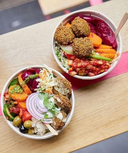two vegan falafel bowls with colorful salads on a wood table at maoz vegetarian
