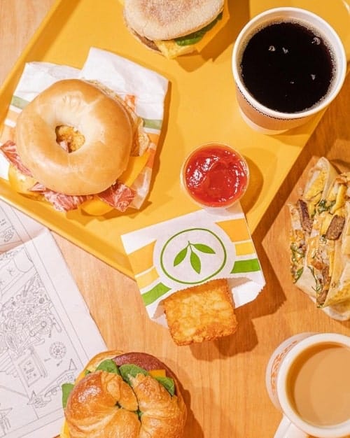 a spread of vegan breakfast sandwiches next to two cups of hot coffee on a wood table at plant power fast food in las vegas