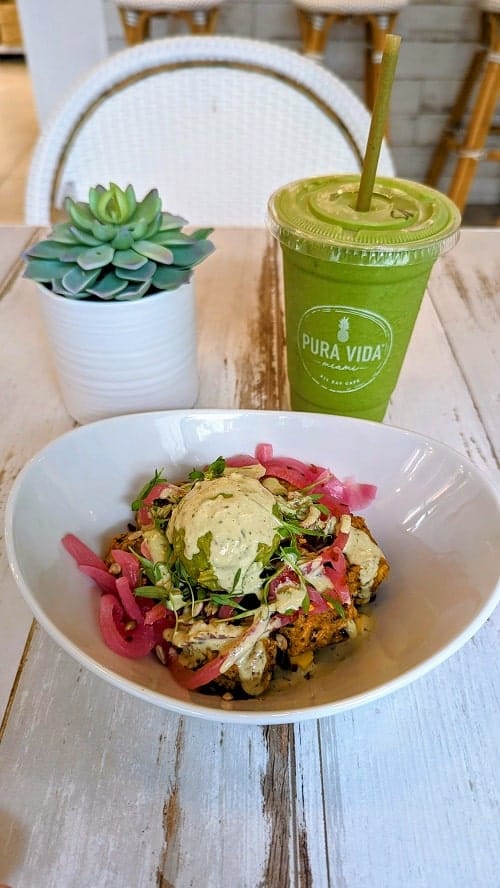 vegan spicy veggie bites covered in avocado and cream sauce next to a green smoothie at pura vida in west palm beach