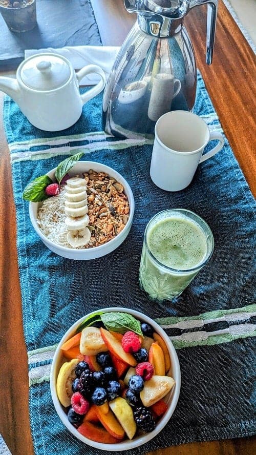 vegan room service spread with a bowl of tropical fruit, green smoothie, oatmeal topped with bananas and coffee at the palmaia resort