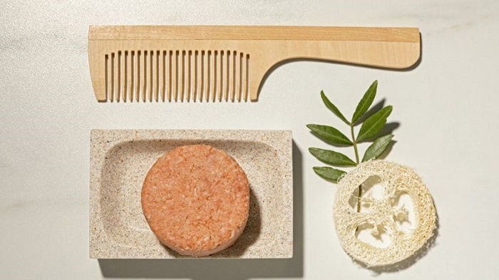 shampoo bar sitting on a holder next to a wooden comb on a neutral background