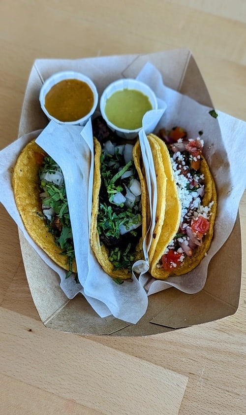 three vegan tacos next to each other in a paper tray with a red and green sauce at tacotarian in las vegas