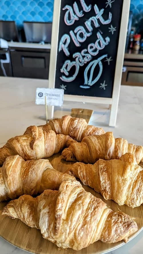 a plate of golden vegan croissants in front of a sign that says plant based at the palmaia resort in playa del carmen
