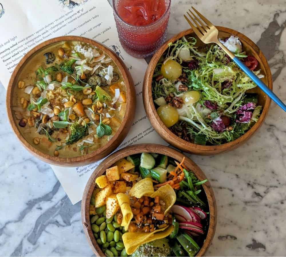 three colorful vegan bowls next to a red drink on a marble table at the vegan restaurant ve by subculture in west palm beach