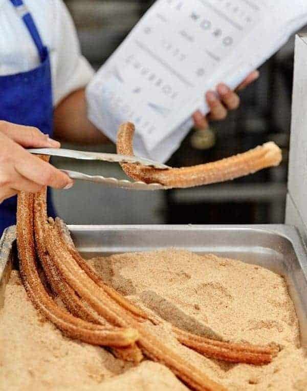 a person putting freshly made vegan churros into a white paper bag in mexico city