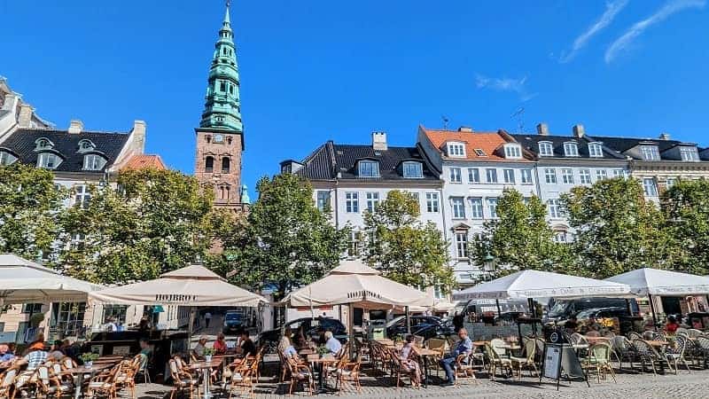 cafe umbrellas in a square in copenhagen surrounded by old buildings and trees