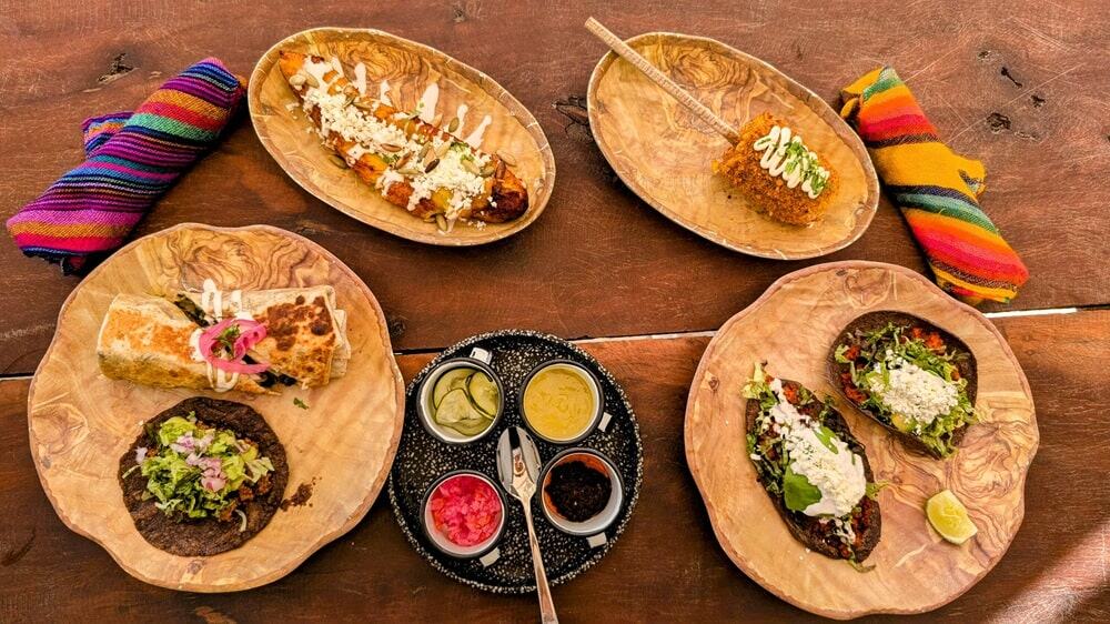 a spread of vegan tacos next to corns on the cob covered in a cream sauce and a bakes plantain on a picnic taco at charlys tacos at the palmaia resort