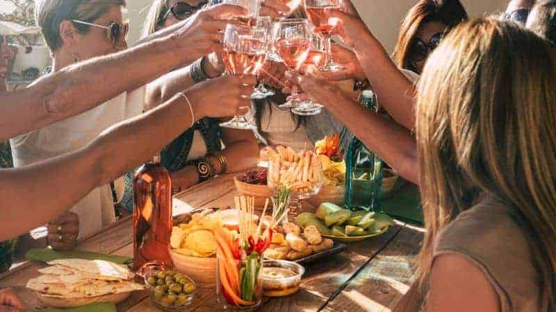 people drinking wine and cheersing in celebration over a table of food