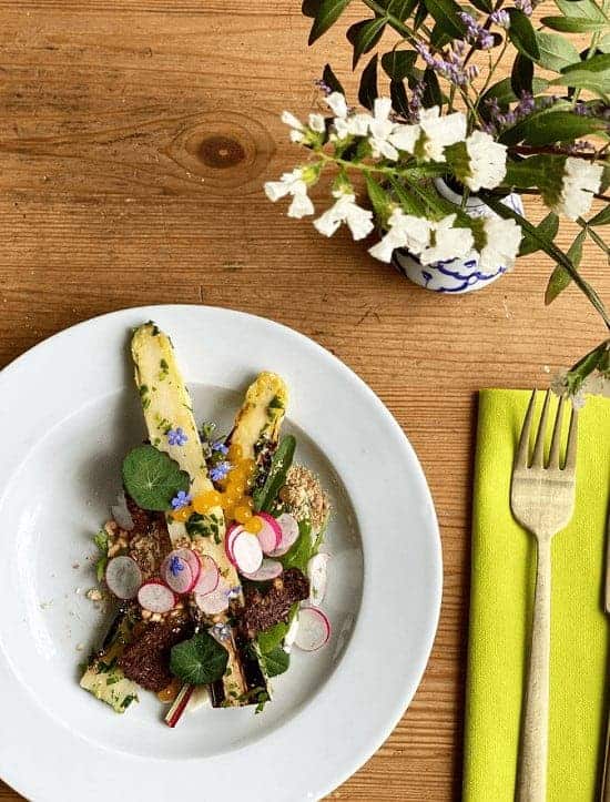 roasted green asparagus topped with sliced radish  next to white flowers at urten in copenhagen