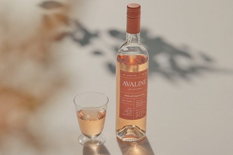 a bottle of vegan rose with a pink label next to a small glass of rose on a light and shady background