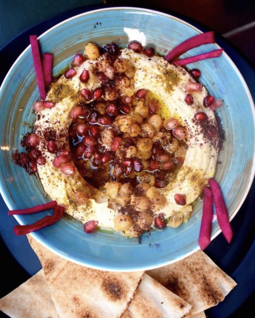 Vegan hummus dish at Maha Brussels topped with chickpeas, pomegranate seeds, spices, and olive oil, served with warm pita bread.