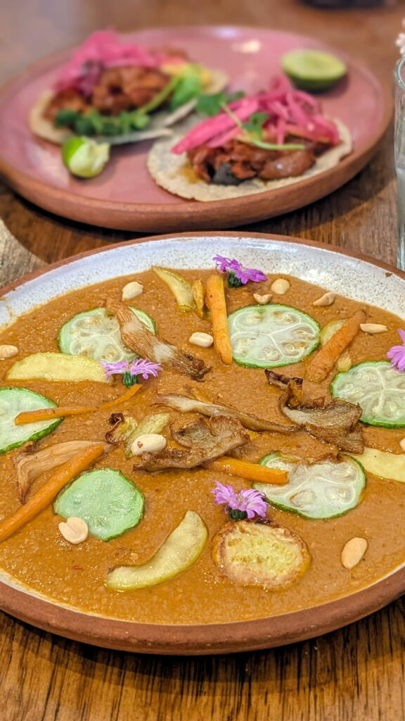 bright orange vegan mexican mole with tacos in the background at Na Tlali