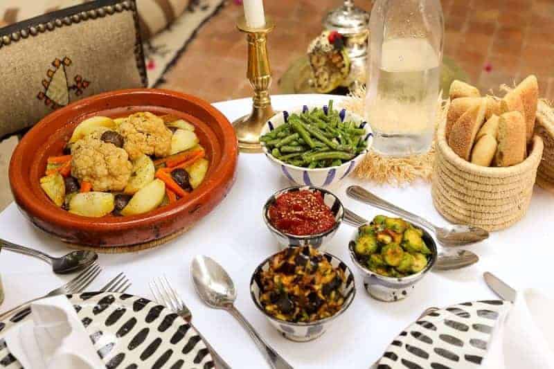 vegan dinner spread with a vegetable tajine, bread, and salads on a white table clothed table at the riad dar zaman in morocco