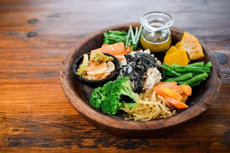 a colorful veggie bowl with a side of dressing on a wood table at the vegan-friendly yoga retreat yogabarn in bali