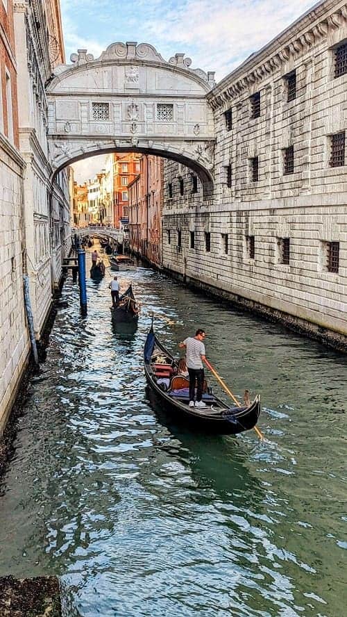 gondaliers paddling down a canal under the bridge of sighs in venice