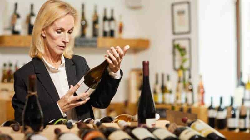 a woman looking at the label of a bottle of wine in a wine store