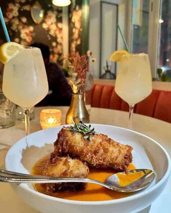 two pieces of crispy vegan chicken on a white plate between two lemon cocktails at cadence in NYC