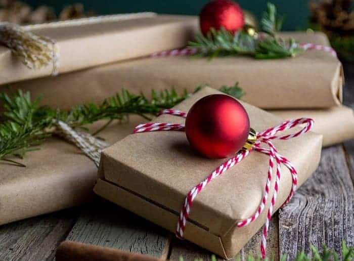 a brown paper package wrapped with red and white ribbon with a red ornament on top