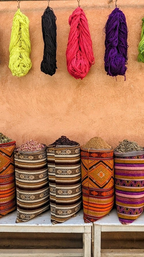 colorful sacks of spices beneath spools of brightly colored yarn on a tan wall in morocco