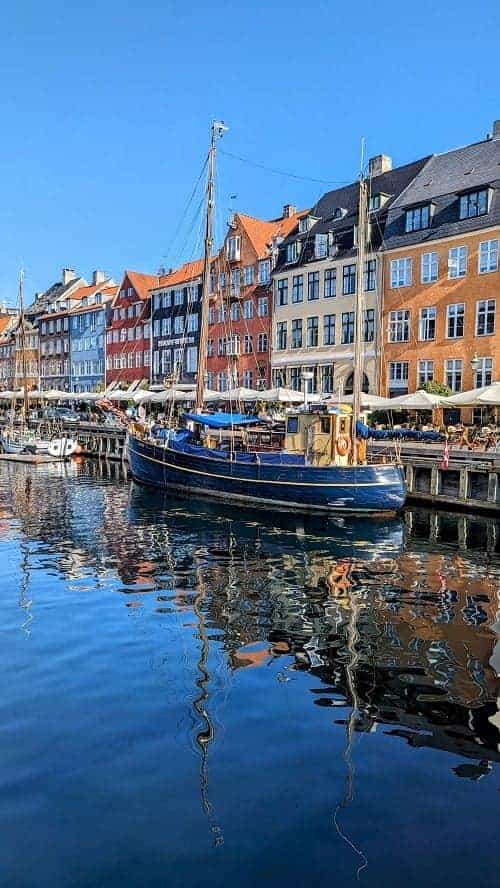 the copenhagen harbor surrounded by colorful tall buildings with one boat sitting along the waters edge