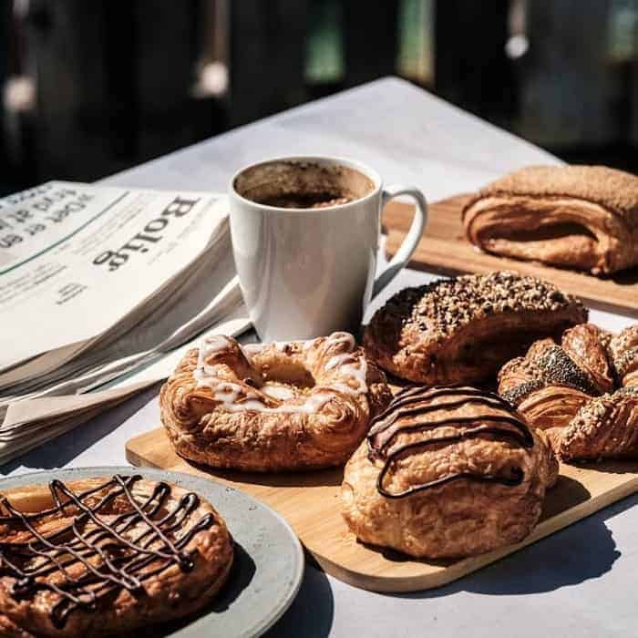 a spread of vegan pastries and bread next to a coffee mug in the sun at det rene brød copenhagen-min