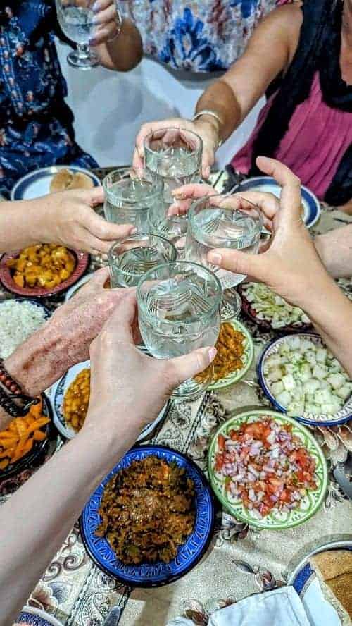 a group of people cheersing with their water glasses over a spread of vegan salads in morocco