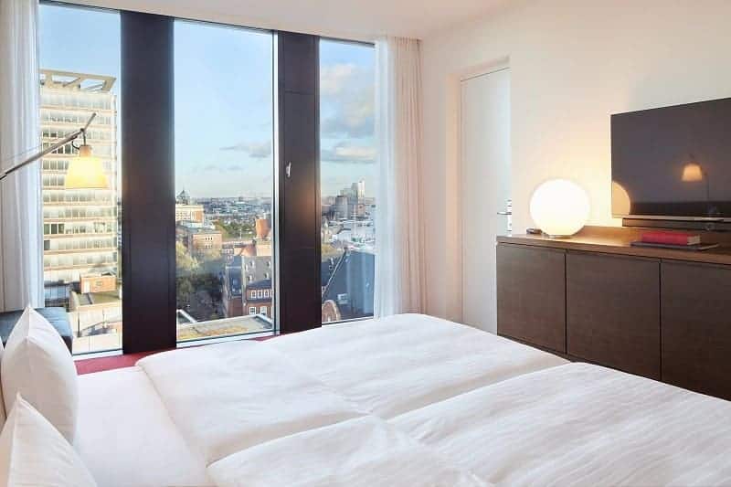 a single guestroom with a white duvet covered bed with a view of hamburg at the empire riverside hotel