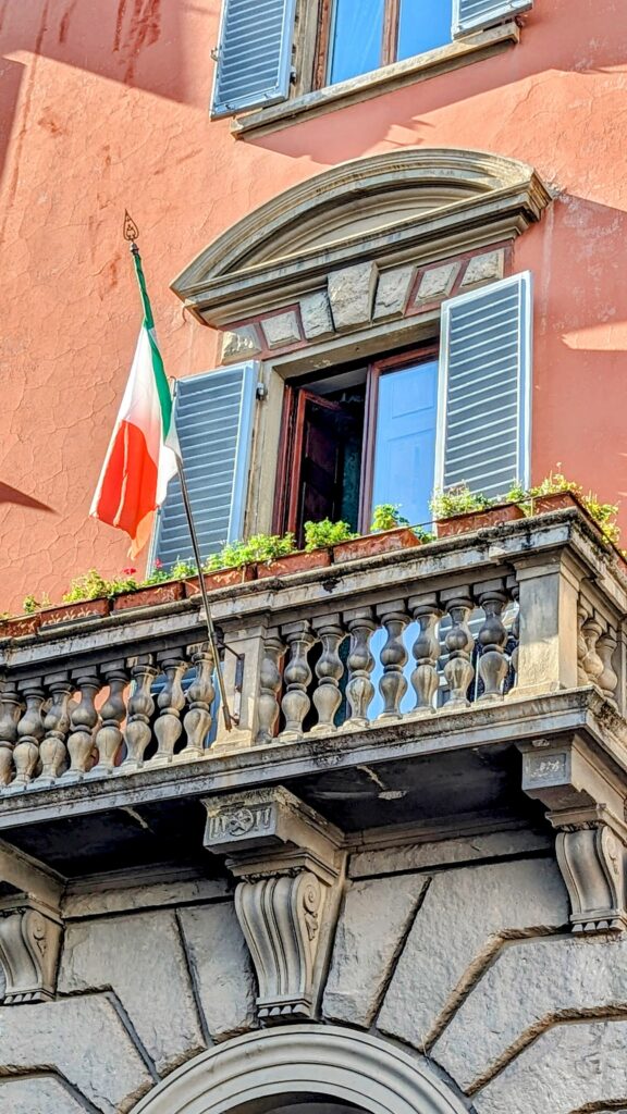 an orange building with an ornate balcony with an italian flag