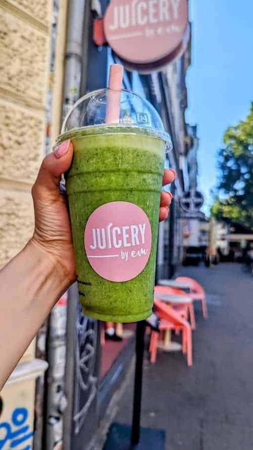 green vegan smoothie held in front of the pink sign for juicery by em in hamburg
