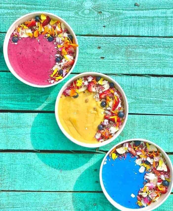 three brightly colored vegan smoothie bowls sitting on a diagonal on a turquoise table at ibiza bowls in copenhagen 
