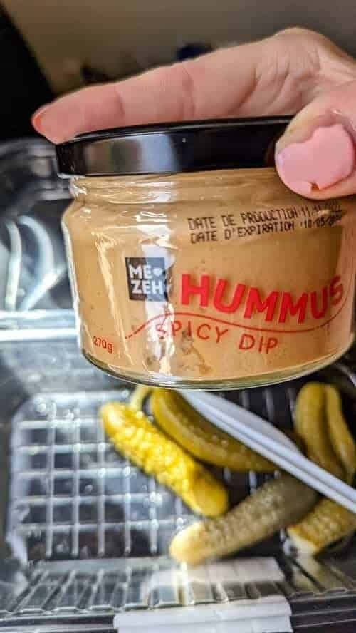 jar of hummus held over a small dish of pickles 