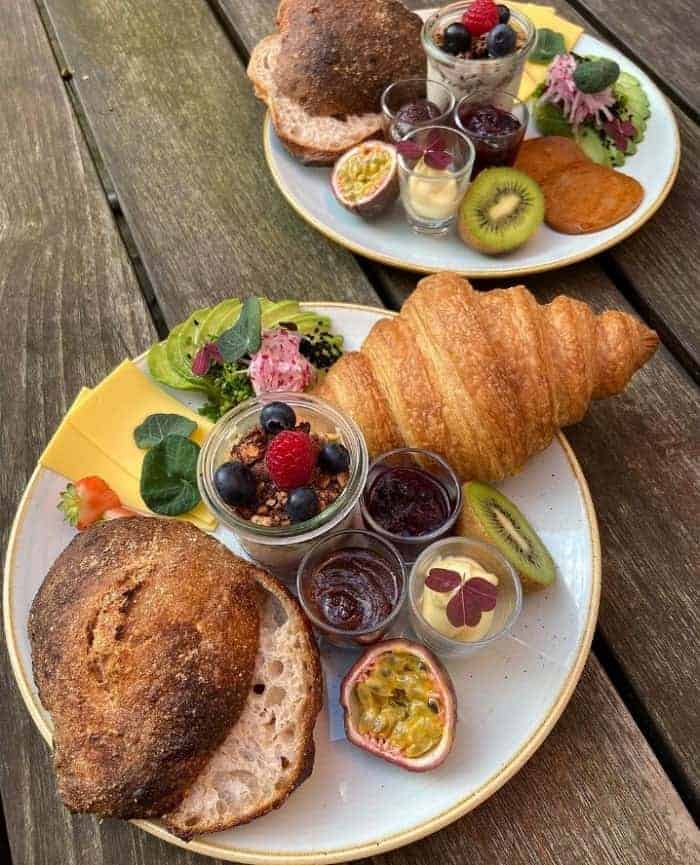 vegan croissant, fruit, and a roll on two white plates on a picnic table at kaf in copenhagen