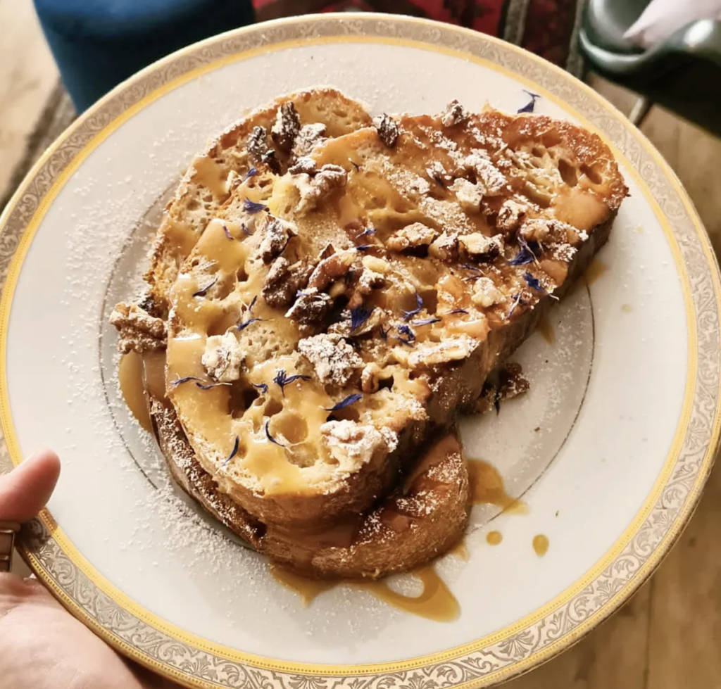 Vegan French toast at L’Alchimiste Brussels topped with caramelized fruit, nuts, and powdered sugar on a vintage plate.
