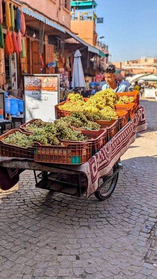 a man pushing a large cart of green grapes through the medina in marrakech