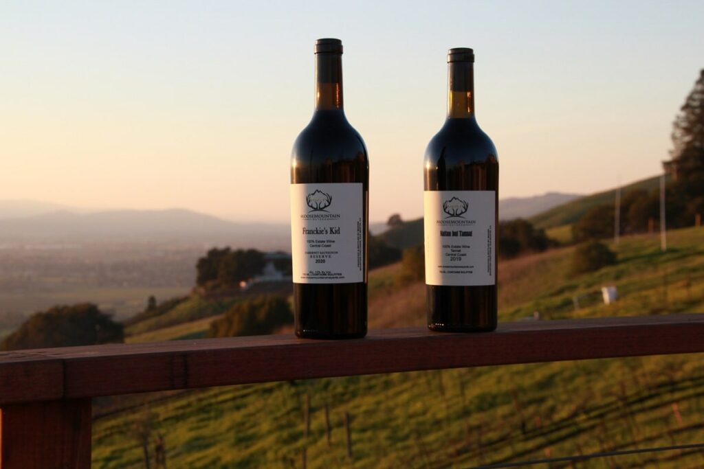 two bottles of vegan moose mountain vineyards wine standing on a grassy hill at sunset