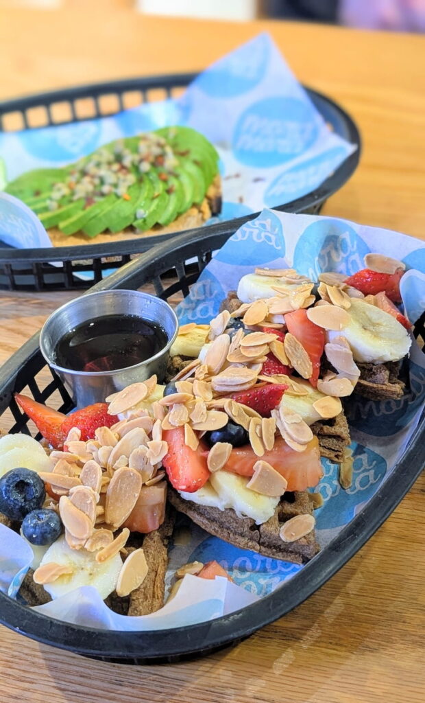 a black basket with four pieces of vegan belgian waffle topped with berries and almonds