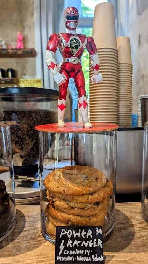 a red power ranger figurine standing on top of a cookie jar with vegan cookies inside at nasch in hamburg