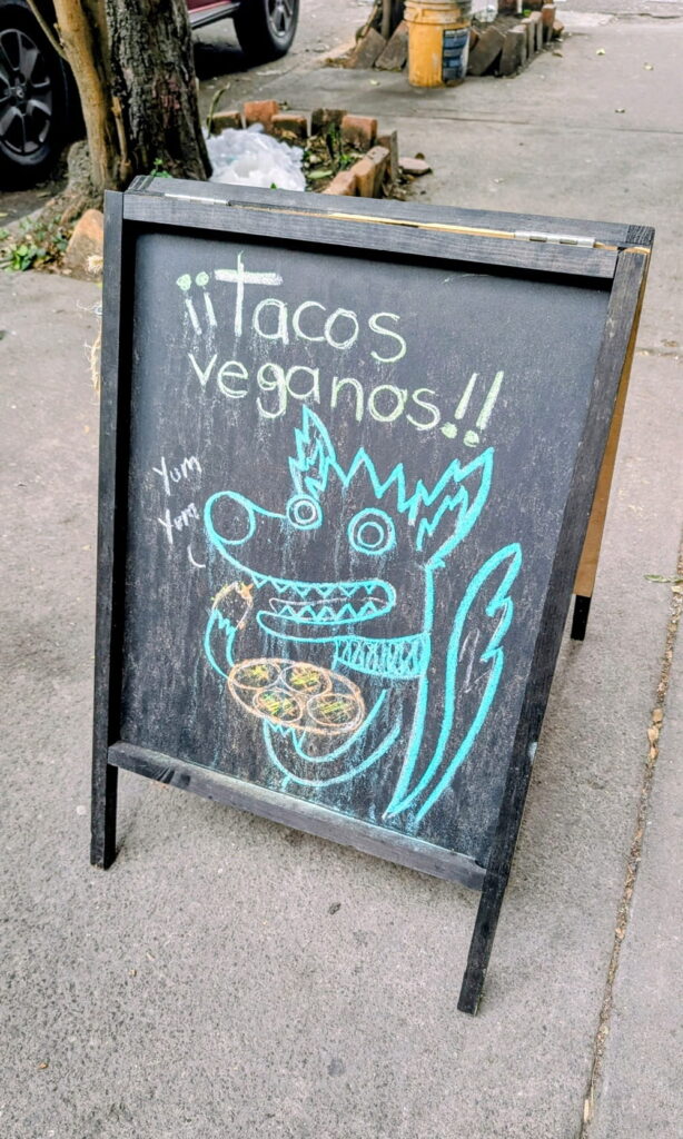 a black chalk board that says vegan tacos with a dog in spanish
