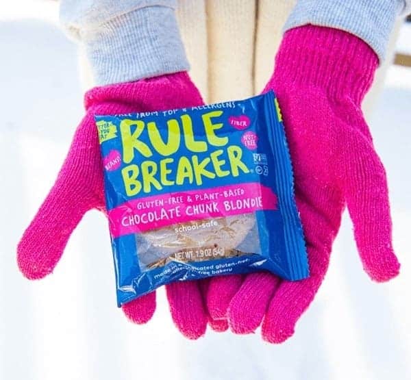 vegan cookie/blondie treat in blue packaging being held by someone where bright pink gloves in the wintertime