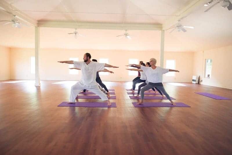 multiple people all holding the same yoga pose and dressed in white inside of a bright room in north carolina